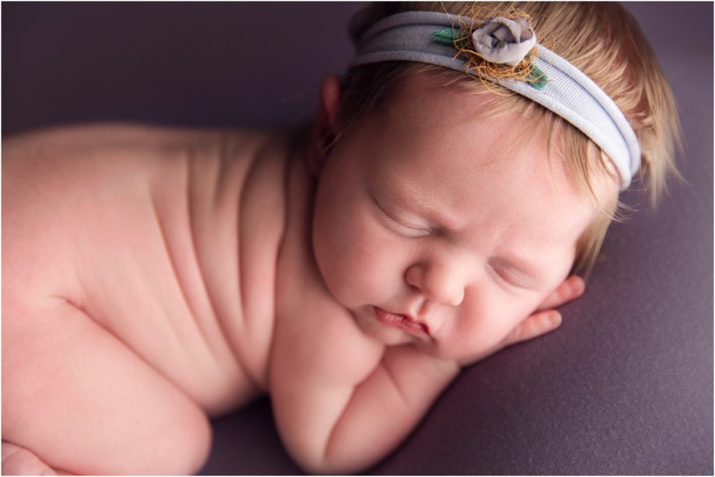 Newborn girl with Blonde Hair on Purple Backdrop